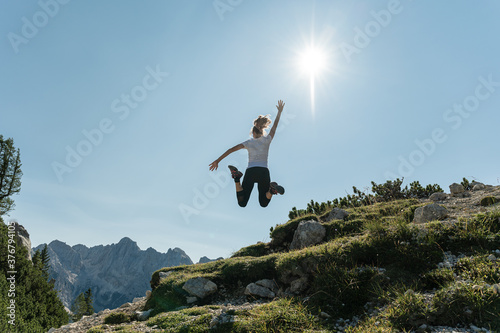 Young female hiker jumping up high enjoying life and the beautiful view of mountains