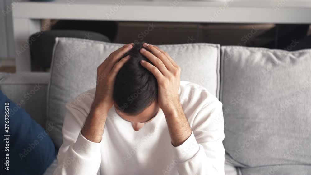 Depressed caucasian man feeling loser worrying about problem sitting alone on the couch at home. Nervous anxious young guy looking frustrated suffering from stress, concerned about the remorse concept Depressed caucasian man feeling loser worrying about problem sitting alone on the couch at home. Nervous anxious young guy looking frustrated suffering from stress, concerned about the remorse concept