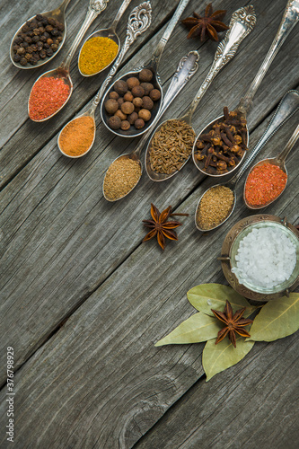 Different spices, seasonings in spoons on a wooden background.