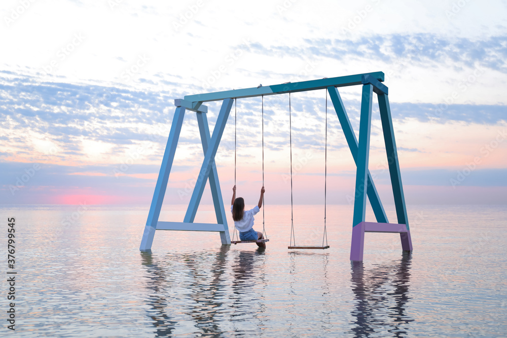 Young woman enjoying sunrise on swing over water Young woman enjoying sunrise on swing over water