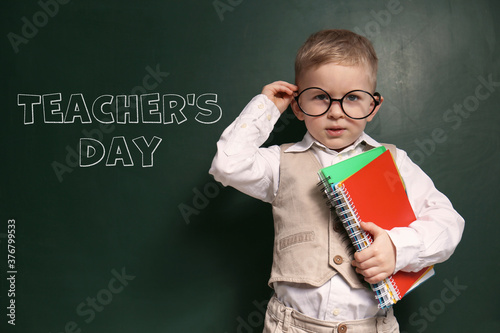 Cute little child wearing glasses near chalkboard with text Teacher's Day photo