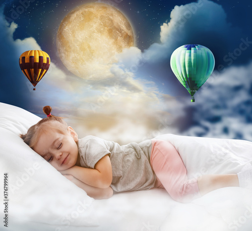 Cute little girl sleeping in bed. Full moon and hot air balloons in cloudy sky - sweet dreams
