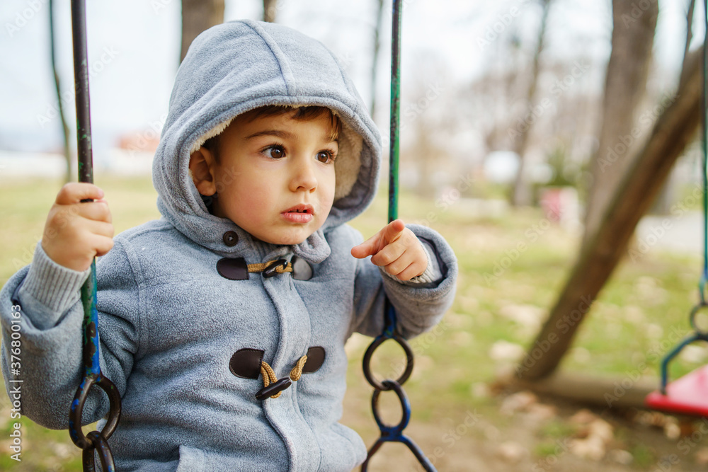 Side view on small caucasian boy in winter coat swinging in park having fun alone in autumn day - copy space leisure activity growing up concept Side view on small caucasian boy in winter coat swinging in park having fun alone in autumn day - copy space leisure activity growing up concept