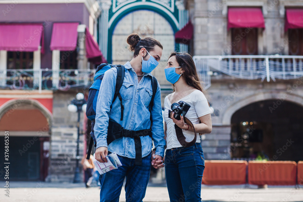 Tourist couple in a historical latin american city with face mask holding a camera on vacation in coronavirus pandemic