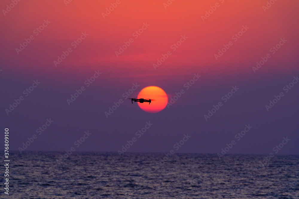 美しい海と夕陽に重なるドローン