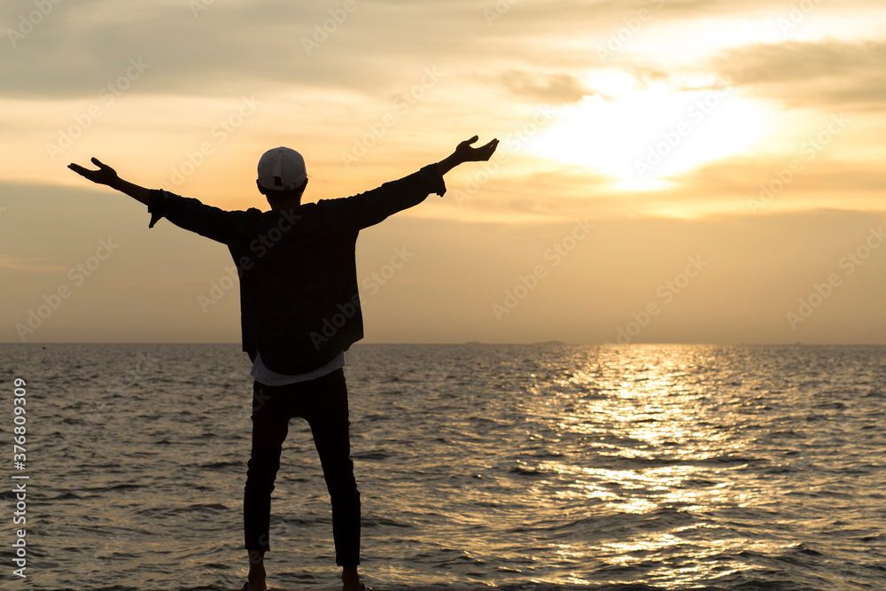silhouette of man standing on the beach and arms raised to happy at sunset, Happy,  freedom and relaxing concept