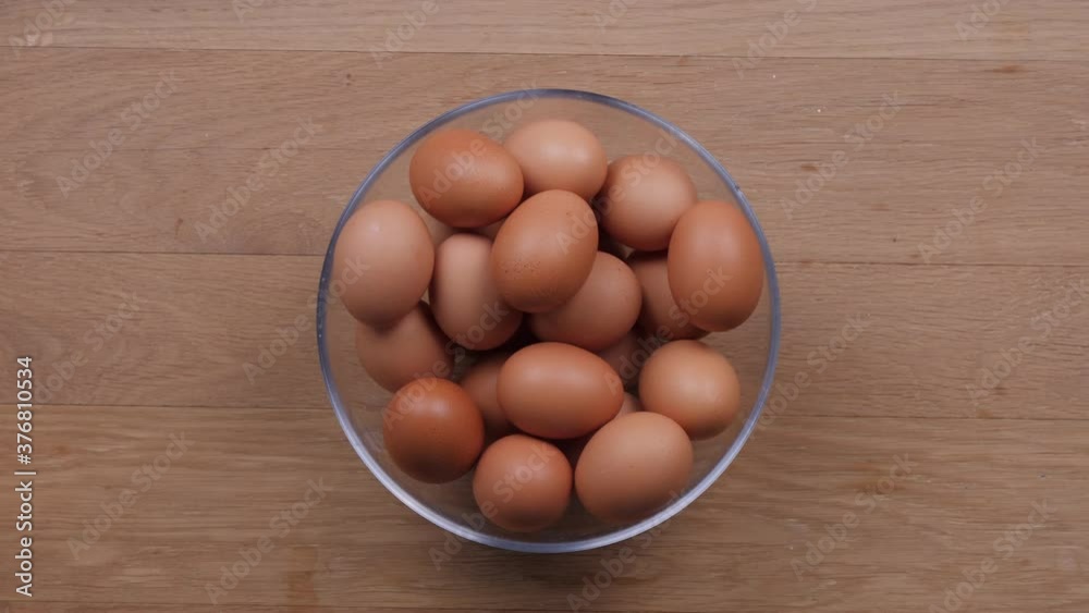 Putting bowl full of eggs on wooden table, static top view. Putting bowl full of eggs on wooden table, static top view.