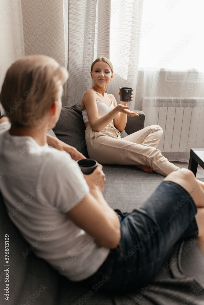 a beautiful woman and a man are sitting on the sofa, chatting and drinking tea. Pleasant conversation of a young couple.