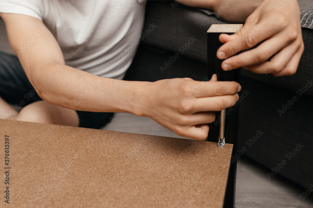 Obraz premium a man in casual clothes is screwing a screw into the table with a screwdriver. Close-up. Family everyday life.