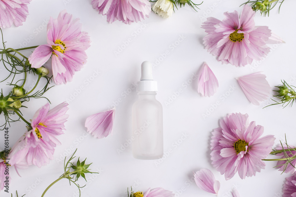 Glass bottle with pipette next to fresh flowers and petals on white background. Natural beauty product. Flat lay, top view. Glass bottle with pipette next to fresh flowers and petals on white background. Natural beauty product. Flat lay, top view.