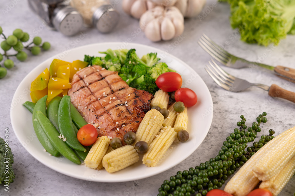 Chicken steak topped with white sesame, peas, tomatoes, broccoli and pumpkin in a white plate. Chicken steak topped with white sesame, peas, tomatoes, broccoli and pumpkin in a white plate.