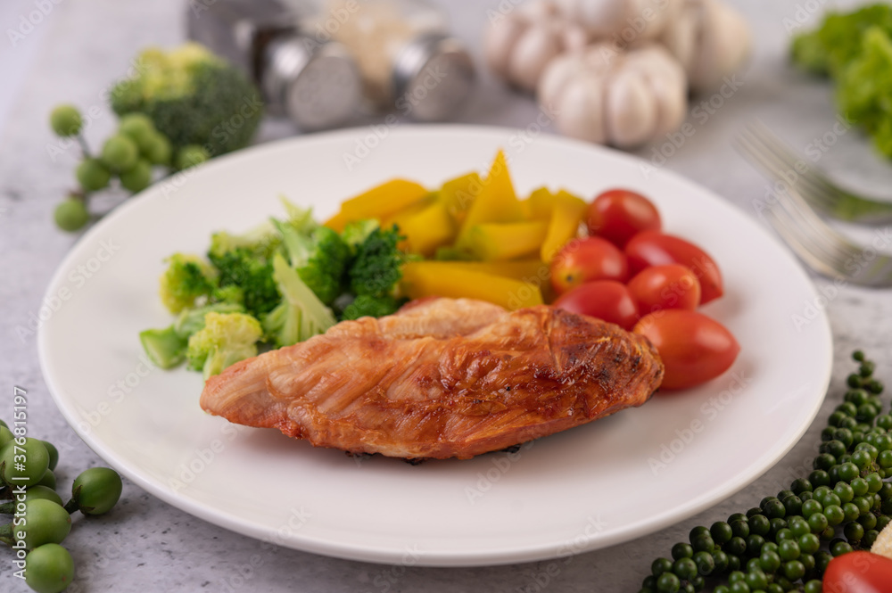 Chicken steak topped with white sesame, peas, tomatoes, broccoli and pumpkin in a white plate.