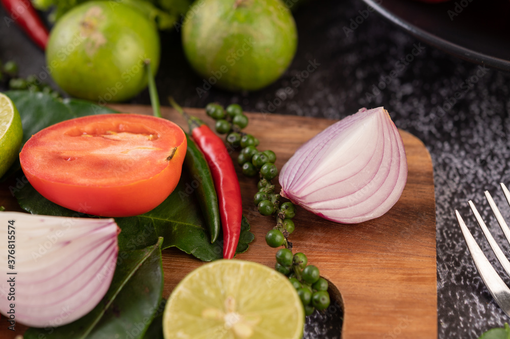 Onion, chili, fresh pepper Kaffir lime leaves and lime placed on a wooden chopping board.