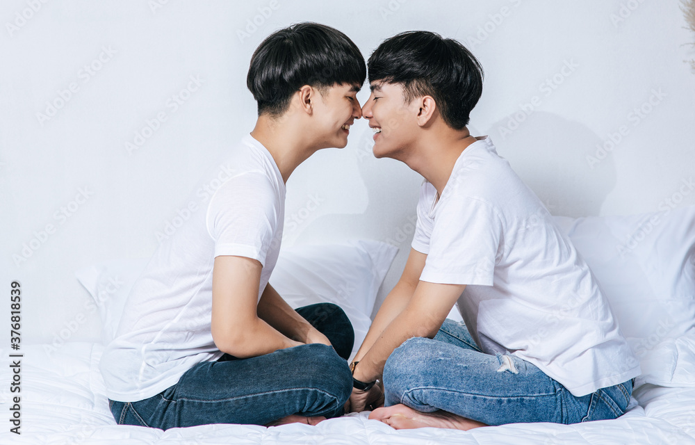 Two dear young men were sitting on the bed, holding hands and looking at each other. Two dear young men were sitting on the bed, holding hands and looking at each other.