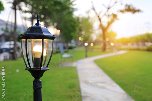 Canvas Print Close up europe style pole of lamp with light on in green grass field at evening