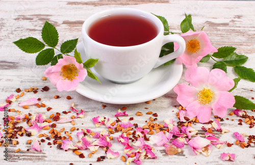 Cup of tea with wild rose flower on old rustic wooden background