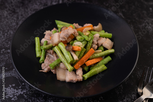 Stir-fried long beans and carrots, add pork belly, put on a black plate.