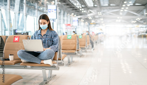 digital nomad and freelance lifestyle concepts.Young asian woman wearing face mask using laptop computer working and sitting with distance during coronavirus 2019 outbreak at airport terminal © Yingyaipumi