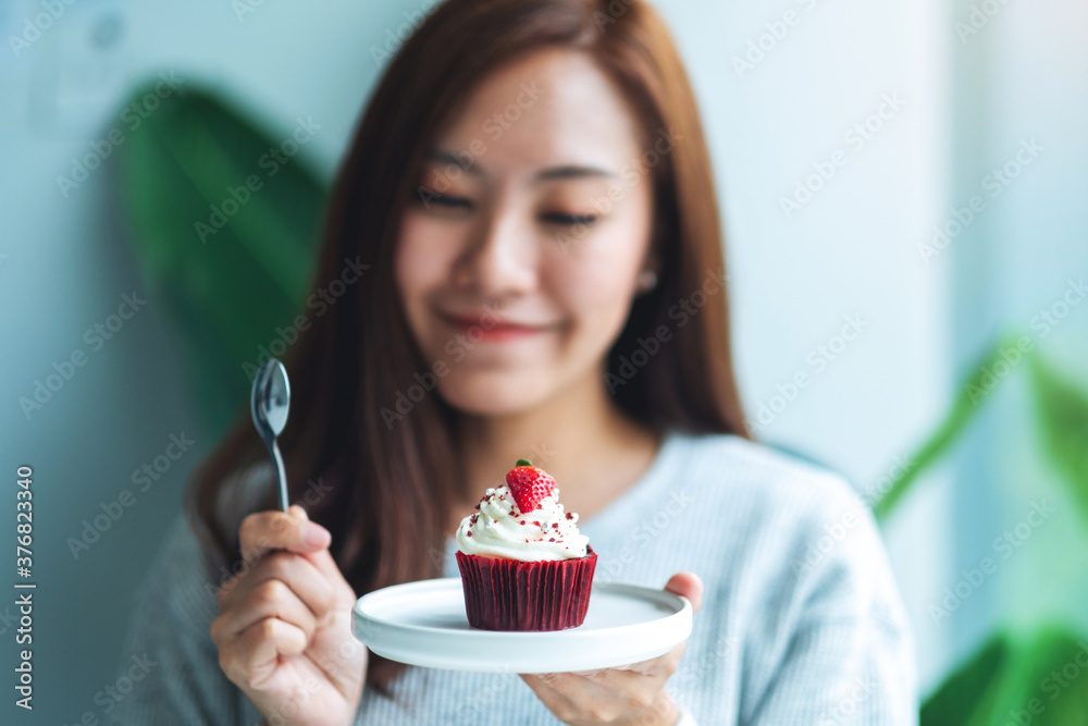 A beautiful asian woman holding and eating a red velvet cup cake