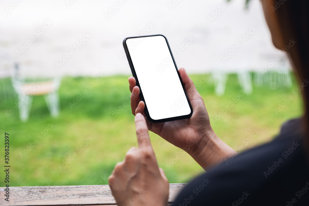 Mockup image of a woman holding and touching on mobile phone with blank white desktop screen