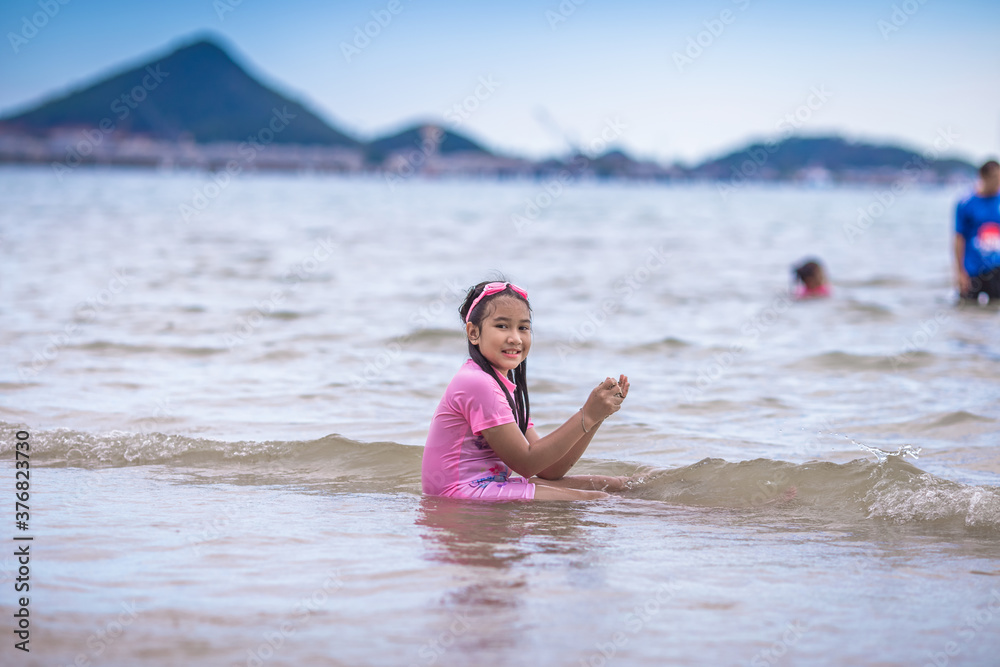 Close-up background view of an Asian girl, playing in the sea on the beach, with a parent or guardian supervising during the holidays, family getaways. Close-up background view of an Asian girl, playing in the sea on the beach, with a parent or guardian supervising during the holidays, family getaways.