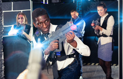 Portrait of African Americanman playing laser tag with his co-workers on dark arena