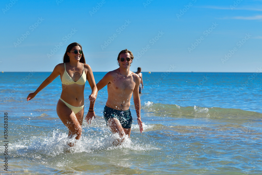 Young couple walking in the sea while smiling and looking at the camera on an out of focus background. New holidays and couples concept.