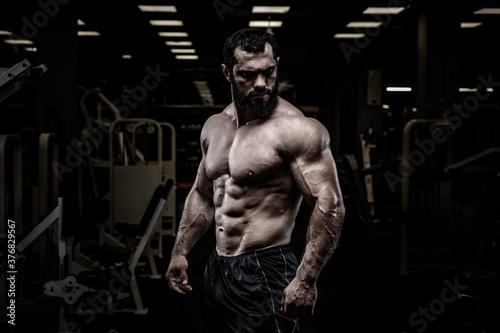 handsome healthy young strong bearded caucasian man with perfect sport physique body in dark athlete gym