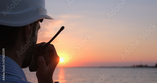 Close-up of an engineer talking into a walkie-talkie and looking towards the sea at dawn. photo