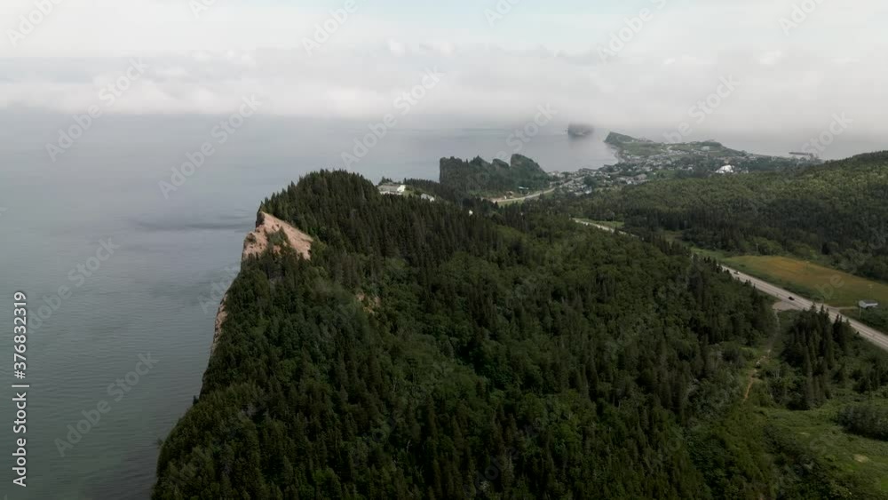 Lush Green Forest Of Gaspe Peninsula Overlooking The Perce Rock On The Distance On A Foggy Day In Quebec, Canada. - aerial drone Lush Green Forest Of Gaspe Peninsula Overlooking The Perce Rock On The Distance On A Foggy Day In Quebec, Canada. - aerial drone