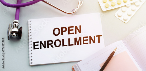 OPEN ENROLLMENT text written in a notebook lying on a medicine desk and a stethoscope. Medical concept.