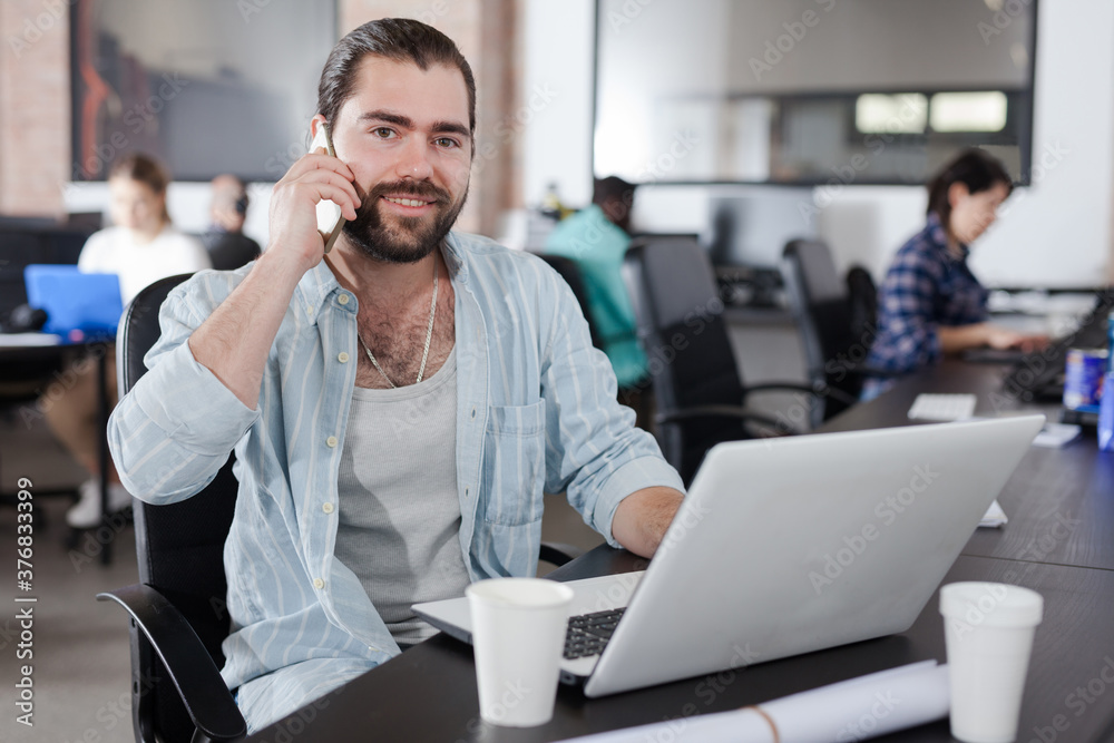 Obraz premium Happy young freelancer having phone call conversation at workplace in coworking space..