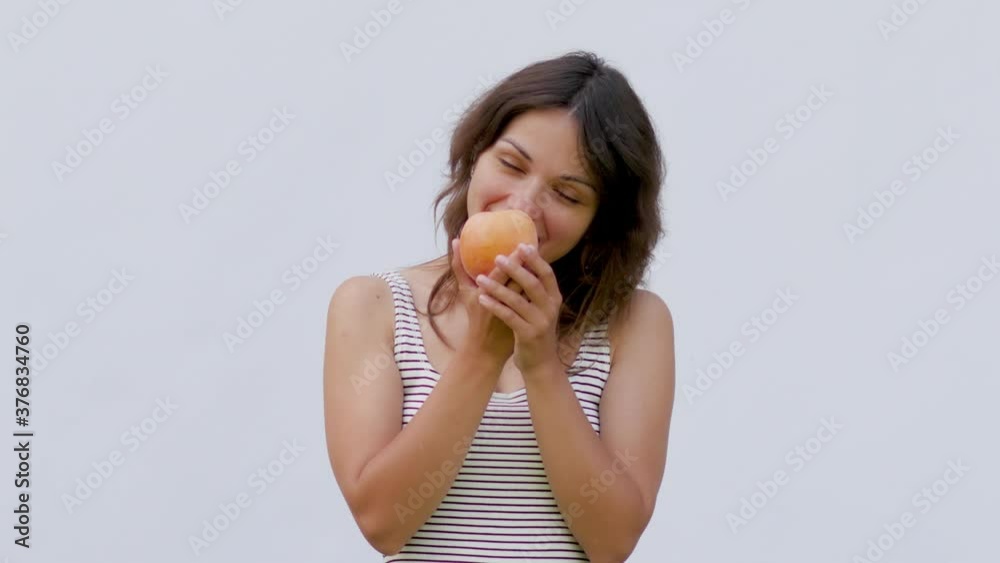 young attractive woman on a white background holding a peach. woman eating peach on white background young attractive woman on a white background holding a peach. woman eating peach on white background