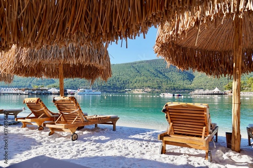 Bamboo umbrellas on a white beach with emerald water, yachts and green hills in the background. Happy Luxury Tourism conception
