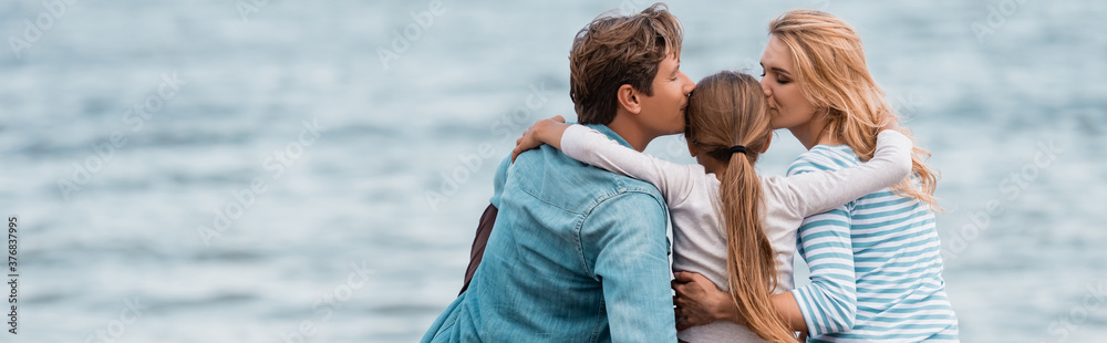 Horizontal crop of parents kissing daughter near sea - obrazy, fototapety, plakaty 