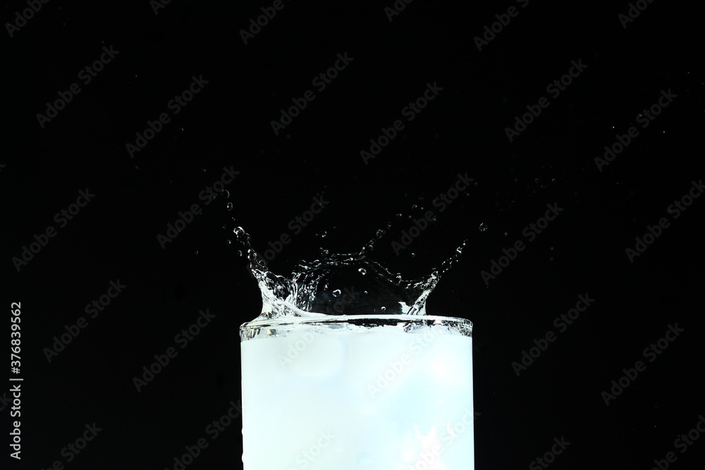 Splash from ice cube in a glass of water, isolated on the black background - obrazy, fototapety, plakaty 