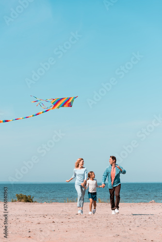 Selective focus of family running with kite on beach during vacation near sea