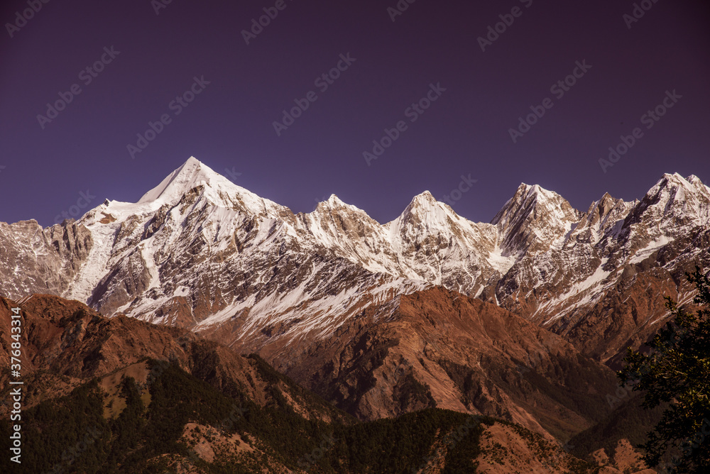 Obraz premium View of Snow cladded Panchchuli peaks falls in great Himalayan mountain range & alpine grass meadows enroute to Khalia Top trekk trail at small hamlet Munsiyari, Kumaon region, Uttarakhand, India.
