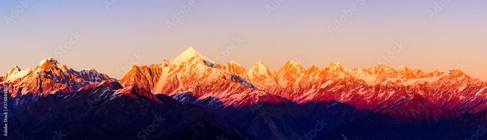 Fototapeta premium Panoramic view during sunset over snow cladded Panchchuli peaks falls in great Himalayan mountain range from small hamlet Munsiyari, Kumaon region, Uttarakhand, India.