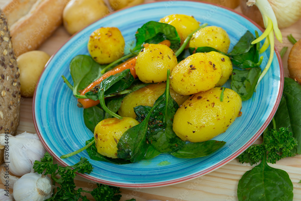 Scene with appetizing roasted new potatoes with spinach and greens
