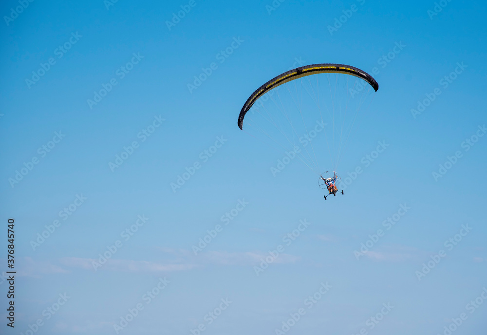 A paraglider with a yellow parachute against a clear blue sky. A paraglider with a yellow parachute against a clear blue sky.