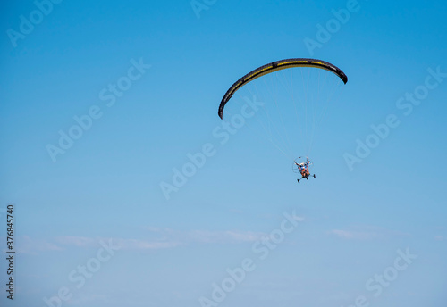 A paraglider with a yellow parachute against a clear blue sky.