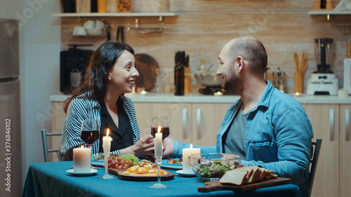 Young man making proposal to his girlfriend during romantic dinner, in the kitchen, sitting at the table drinking a glass of red wine. Surprised engaged celebration fiancee happy woman smiling