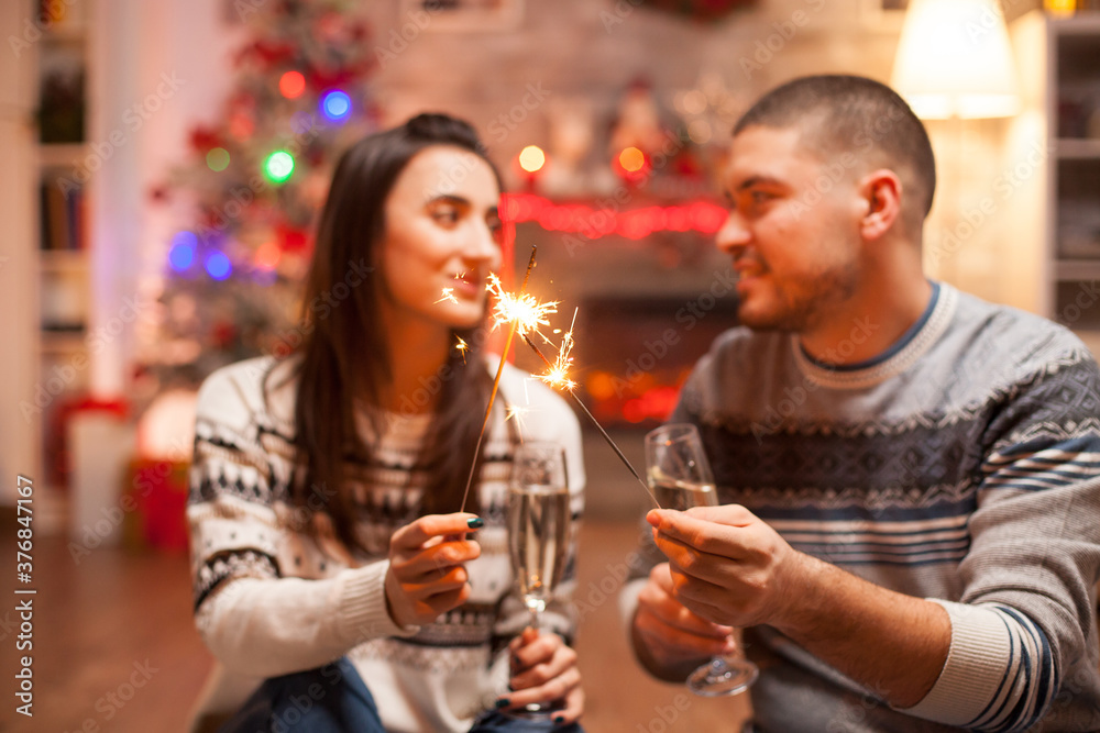Happy couple holding hand fireworks while looking at each other on christmas day.