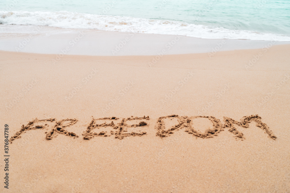 Freedom word hand drawn on sand summer beach.