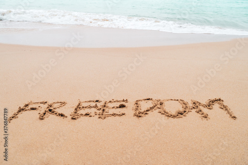 Freedom word hand drawn on sand summer beach.