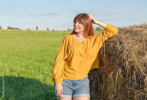 female model plus size on a field with haystacks, a beautiful young woman with brown hair in short shorts and a white shirt, harvest concept © klavdiyav