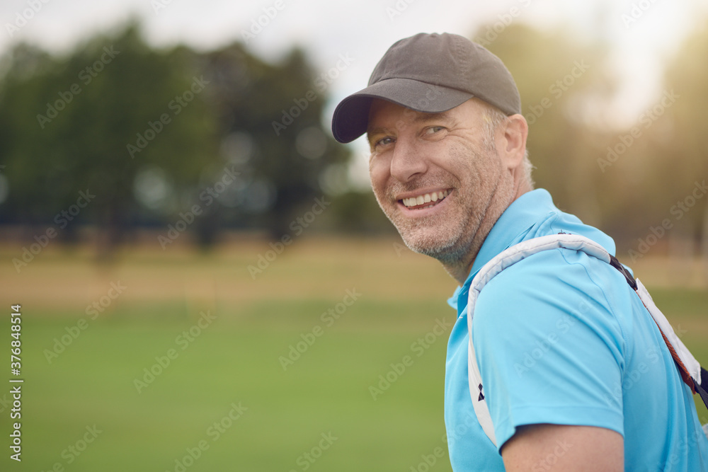 Smiling friendly middle-aged golfer turning to look back over his shoulder at the camera on the fairway or green Smiling friendly middle-aged golfer turning to look back over his shoulder at the camera on the fairway or green