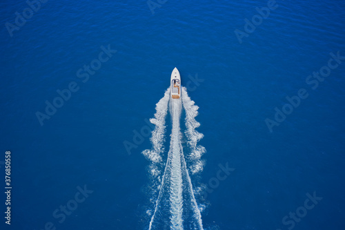 luxury motor boat. Top view of a white boat sailing in the blue sea. Aerial view of a boat in motion on blue water. Drone view of a boat sailing at high speed. © Berg