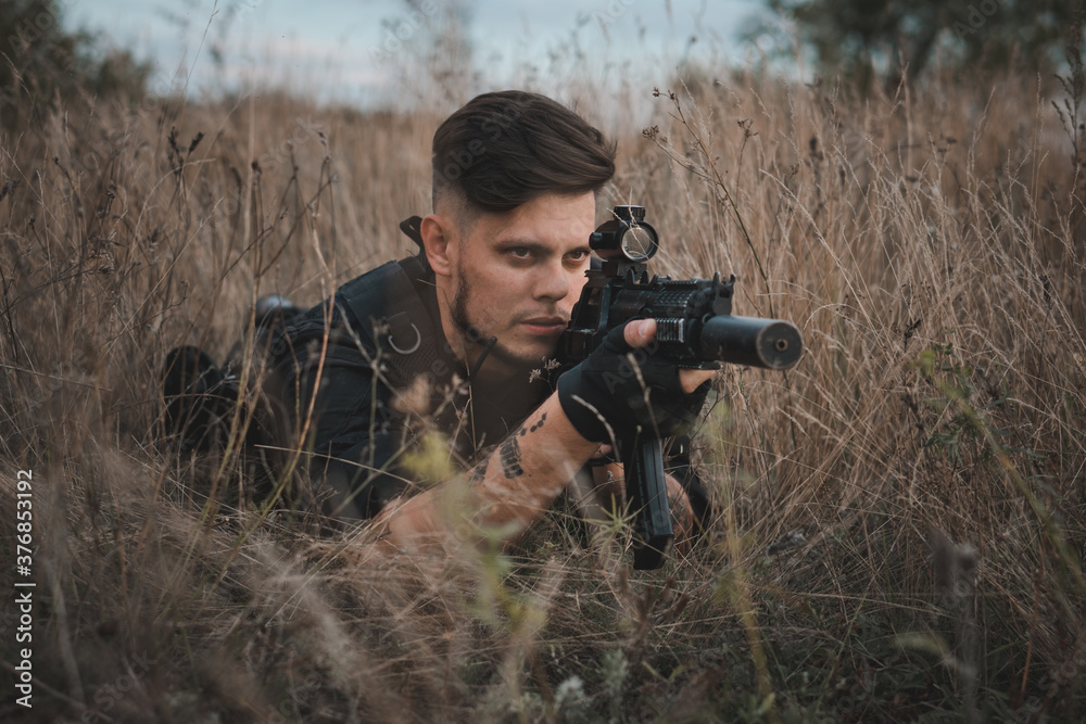 Fototapeta premium Young soldier in black uniform lying down and aiming an assault rifle.